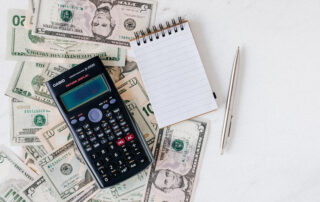 Calculator and notepad placed over stack of usa dollars